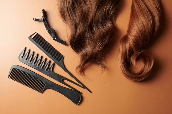 Hairdresser tools close-up isolated on orange background. Curls of brown hair and a set of combs, clips, hairpins, hair beauty salon concept