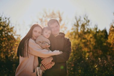 Mutlu aile portresi anne baba ve oğul güneşli bir günde sonbahar parkında birlikte eğleniyor ve eğleniyorlar. Aşk ve sadakat, genç ebeveynler