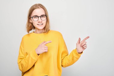 Sarı giysili genç sarışın kız, bir yana, beyaz stüdyo arka grubunda izole edilmiş ürün veya metin için boş alan gösteriyor.