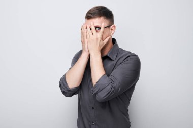 Genç iş adamının portresi, gözleri eliyle kaplayan, beyaz stüdyo arka grubunda izole edilmiş parmaklarıyla dikizleyen