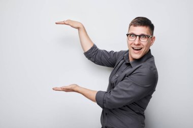 Gözlüklü yakışıklı bir adam elinde bir şey tutuyor. Ürün için boş bir alan ya da beyaz stüdyo arka grubunda izole edilmiş bir mesaj gösteriyor.