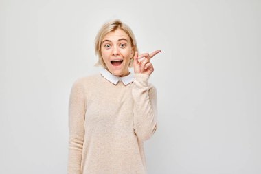 Genç, sarışın bir kadın, gösterişsiz bir şekilde işaret ediyor. Beyaz stüdyo arka grubunda boş bir alan ya da mesaj gösteriyor.