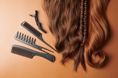 Kuaför aletleri turuncu arka planda izole edilmiş. Kahverengi bukleli saçlar, taraklar, tokalar, tokalar, kuaför salonu konsepti.