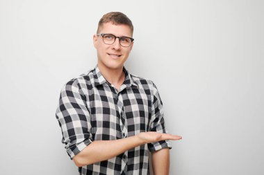 Gözlüklü yakışıklı bir adam elinde bir şey tutuyor. Ürün için boş bir alan ya da beyaz stüdyo arka grubunda izole edilmiş bir mesaj gösteriyor.