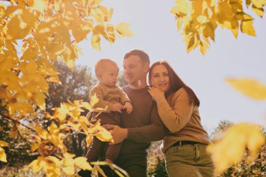 Mutlu aile portresi anne baba ve oğul güneşli bir günde sonbahar parkında birlikte eğleniyor ve eğleniyorlar. Aşk ve sadakat, genç ebeveynler