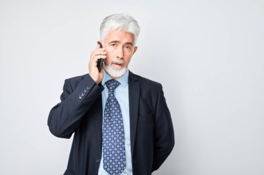 Takım elbiseli yaşlı işadamının cep telefonuyla konuşan portresi. Akıllı telefonu olan kişi beyaz grupta izole edildi