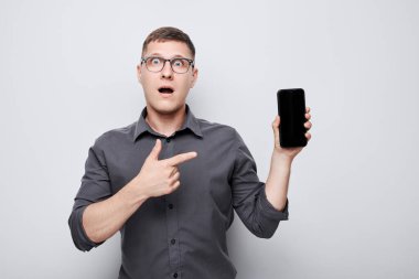 Heyecanlı yüzüyle boş cep telefonu ekranı gösteren genç iş adamının portresi. Akıllı telefonu olan kişi beyaz grupta izole edildi