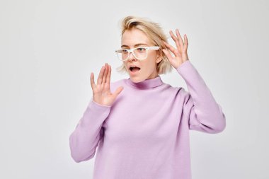 Sarışın genç bir kadının portresi mutlu bir şekilde gülümsüyor avuçlarını kaldırmış ve şok olmuş bir şekilde beyaz stüdyo arka grubunda izole edilmiş ağzı açık.