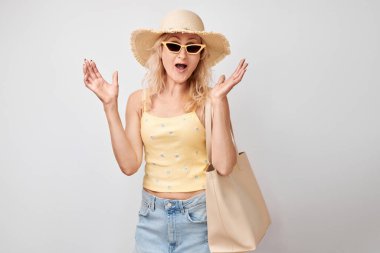 Portre, güneş gözlüklü, şapkalı, alışveriş çantalı, tatilini kutlayan, zıplayan, dans eden, beyaz stüdyoda izole edilmiş, eğlenen olgun sarışın kadın.