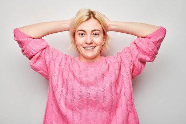 Gülümseyen sarışın genç kadının portresi. Başa dokunan ve sevinen, zaferi kutlayan beyaz stüdyo arka planında izole edilmiş, reklam pankartı.