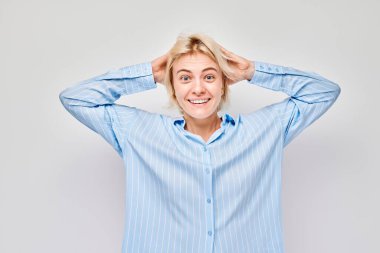 Gülümseyen sarışın genç kadının portresi. Başa dokunan ve sevinen, zaferi kutlayan beyaz stüdyo arka planında izole edilmiş, reklam pankartı.