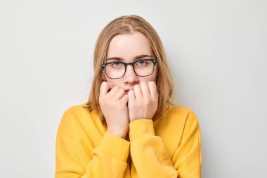 Üzgün yüzlü, beyaz arka planda tırnaklarını yiyen öğrenci kız portresi. Sinirler, stres, belirsizlik.