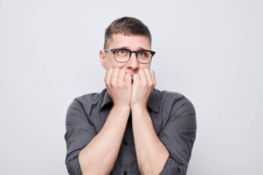 Üzgün suratlı, beyaz arka planda tırnak yiyen bir adamın portresi. Sinirler, stres, belirsizlik.