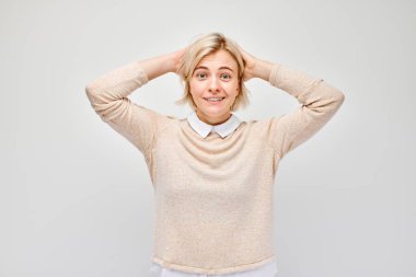 Gülümseyen sarışın genç kadının portresi. Başa dokunan ve sevinen, zaferi kutlayan beyaz stüdyo arka planında izole edilmiş, reklam pankartı.