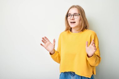 Portre öğrencisi kızın mutlu yüzü, neşeli bir şekilde avuçlarını kaldırarak gülümsüyor ve beyaz stüdyo arka planında izole edilmiş ağzı açık kalmış.