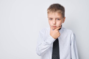Tişörtlü ve kravatlı, elleri çenesinde gri arka planda dalgın genç bir çocuk..
