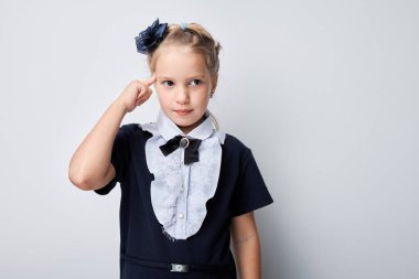 Okul üniformalı, saçları fiyonklu genç bir kızın portresi gri arka planda..