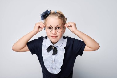 Kız, parlak arka planda yay ve saç bandı ile şık giyinmiş gözlük ayarlıyor.