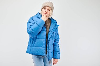 Mavi ceketli ve bereli genç bir kadın beyaz bir arka plana gülümsüyor..