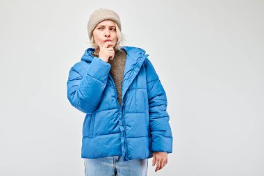 Kış kıyafetli kadın, düşünceli bir ifadeyle, hafif arka planda izole olmayı seçer.