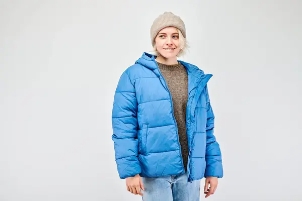 Smiling person in a blue puffer jacket and beanie against a white background.