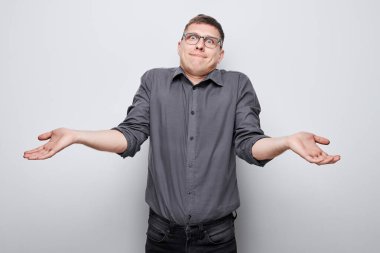 Kafası karışmış genç bir adam gri bir arka plana karşı omuz silkiyor.