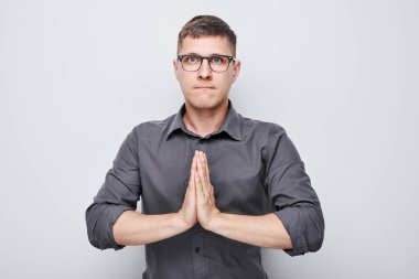 Gözlüklü ve ciddi ifadeli bir adam umutlu bir jest için ellerini birbirine bastırıyor.