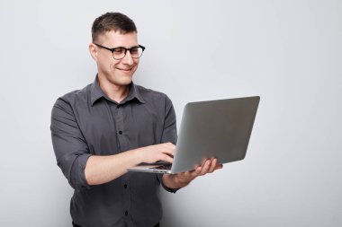 Gözlüklü profesyonel bir adam, gri bir arkaplana karşı dizüstü bilgisayar kullanıyor..