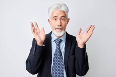 Takım elbiseli kıdemli işadamı, şaşırmış bir ifadeyle, el kaldırıyor, beyaz arka planda soyutlanmış..