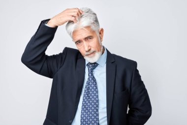 Kafası karışmış işadamı, şüpheyi ve belirsizliği ifade ediyor, gri arka planda izole edilmiş.