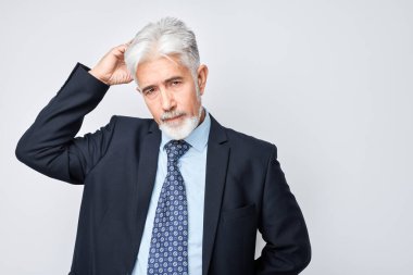 Kafası karışmış işadamı, şüpheyi ve belirsizliği ifade ediyor, gri arka planda izole edilmiş.