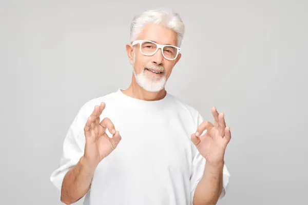Gözlüklü Yaşlı Adam Gri Arka Planda Iyi Bir Jest Yapıyor — Stok fotoğraf
