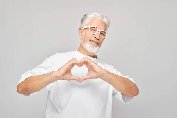 Yaşlı Adam Elleriyle Kalp Yapıyor Gülümsüyor Gri Arka Planda Soyutlanıyor — Stok fotoğraf