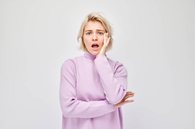 Pembe balıkçı yakalı bir kadın. Elleri yanaklarında şoka girmiş, beyaz bir arka planda izole edilmiş..