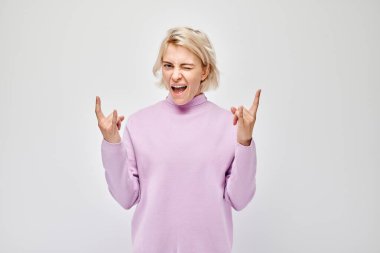 Pembe kazaklı heyecanlı bir kadın beyaz arka planda izole bir şekilde rock 'n roll yapıyor..