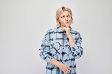 Eli çenesinde, açık gri bir arka planda düşünceli genç bir kadın..