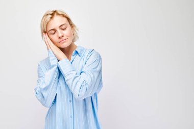 Gözleri kapalı genç bir kadın, hafif arka planda yastık gibi elleriyle uyku jesti yapıyor.