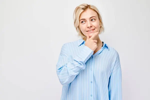 Przemyślana Kobieta Zabawnym Uśmiechem Dotykająca Podbródka Ubrana Niebieską Koszulę Białym — Zdjęcie stockowe