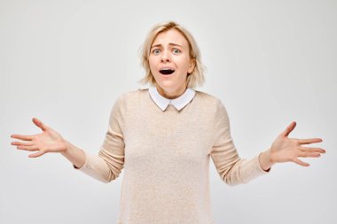 Kafası karışmış genç bir kadın beyaz bir arka planda el hareketi yapıyor..