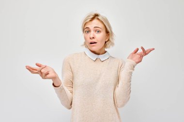 Kafası karışmış genç bir kadın ellerini kaldırarak omuz silkiyor, beyaz arka planda izole edilmiş..