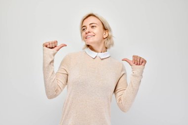 Kendine güvenen bir kadın, arka planda gülümseyen bir başparmakla işaret ediyor..