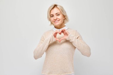 Gülümseyen kadın, elleri ile kalbi şekillendiriyor, beyaz arka planda izole.