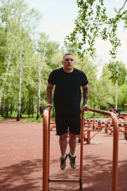 Beyaz tenli erkek sporcu, yaz parkında barfiks çekiyor.