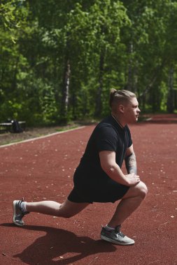 Beyaz erkek sporcu yaz parkında antrenman yapmadan önce ısınma egzersizi yapıyor.