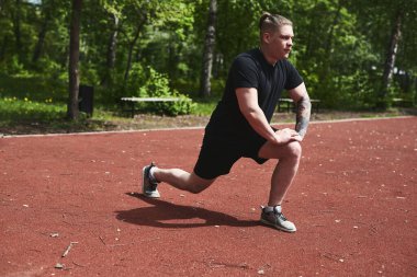 Beyaz erkek sporcu yaz parkında antrenman yapmadan önce ısınma egzersizi yapıyor.