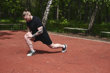Beyaz erkek sporcu yaz parkında antrenman yapmadan önce ısınma egzersizi yapıyor.