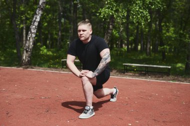 Beyaz erkek sporcu yaz parkında antrenman yapmadan önce ısınma egzersizi yapıyor.