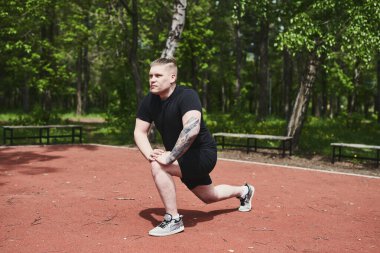 Beyaz erkek sporcu yaz parkında antrenman yapmadan önce ısınma egzersizi yapıyor.