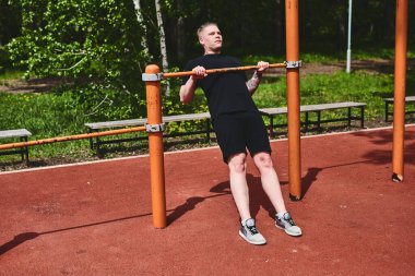 Beyaz tenli erkek sporcu, yaz parkında barfiks çekiyor.