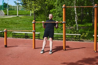 Beyaz tenli erkek sporcu, yaz parkında barfiks çekiyor.